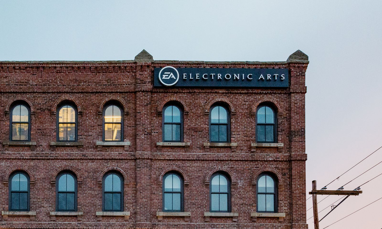 A red brick heritage building with arched windows and an Electronic Arts sign, against a pale sky