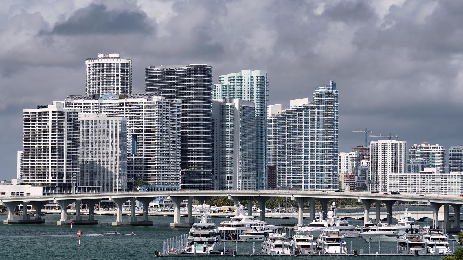 Downtown Miami towers rising over Biscayne Bay with a causeway and a marina full of boats in front