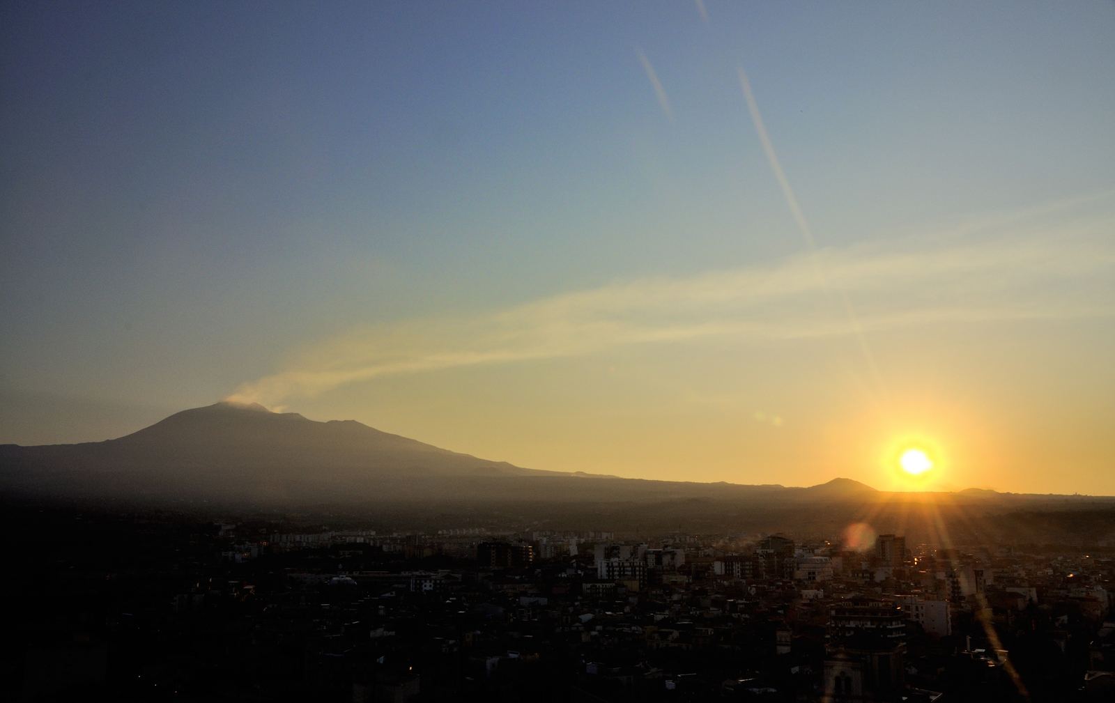 The sun rising beside the long silhouette of Mount Etna over the Sicilian plain at dawn