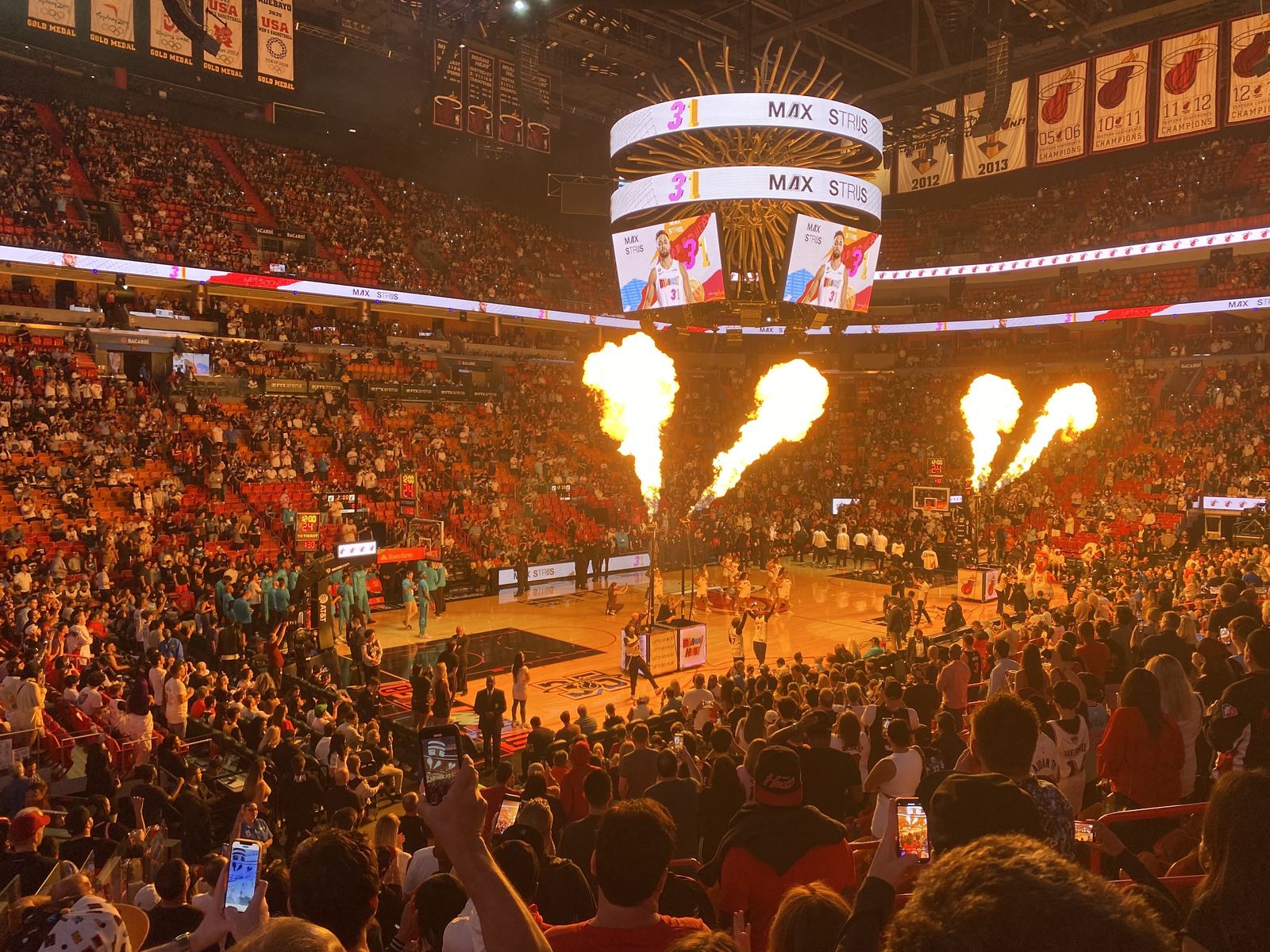 A packed basketball arena glowing orange as flames shoot up during player introductions before an NBA game