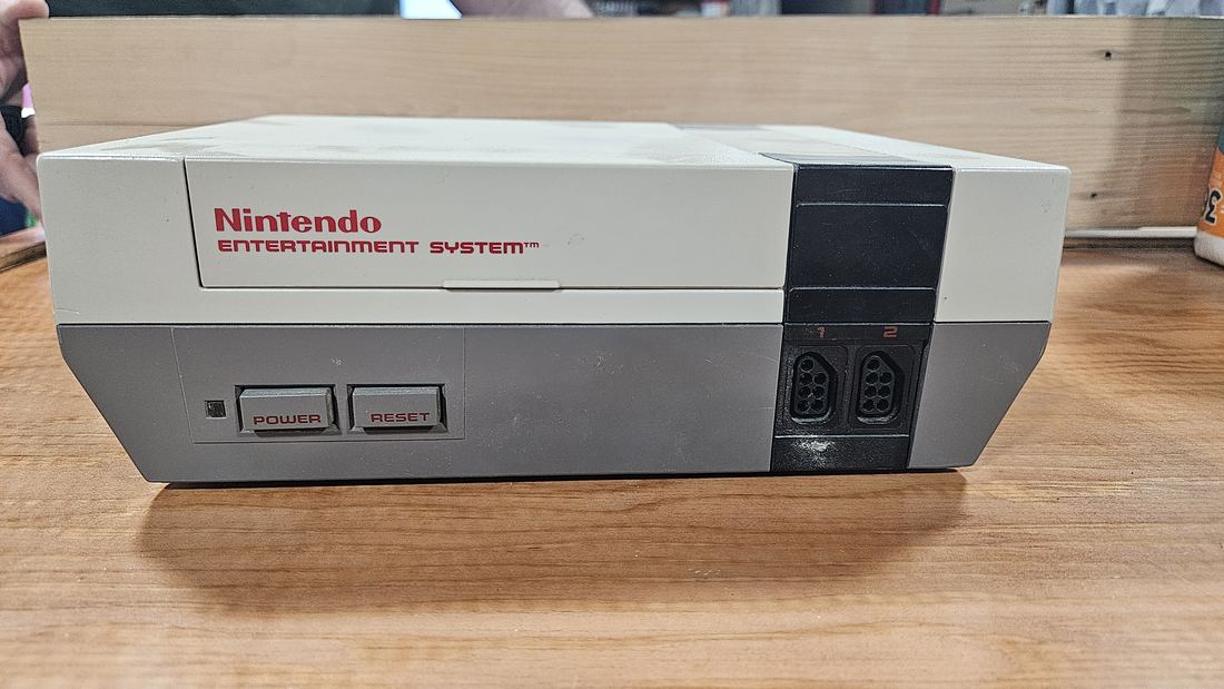 A grey Nintendo Entertainment System console with its red logo and two controller ports, on a wooden table