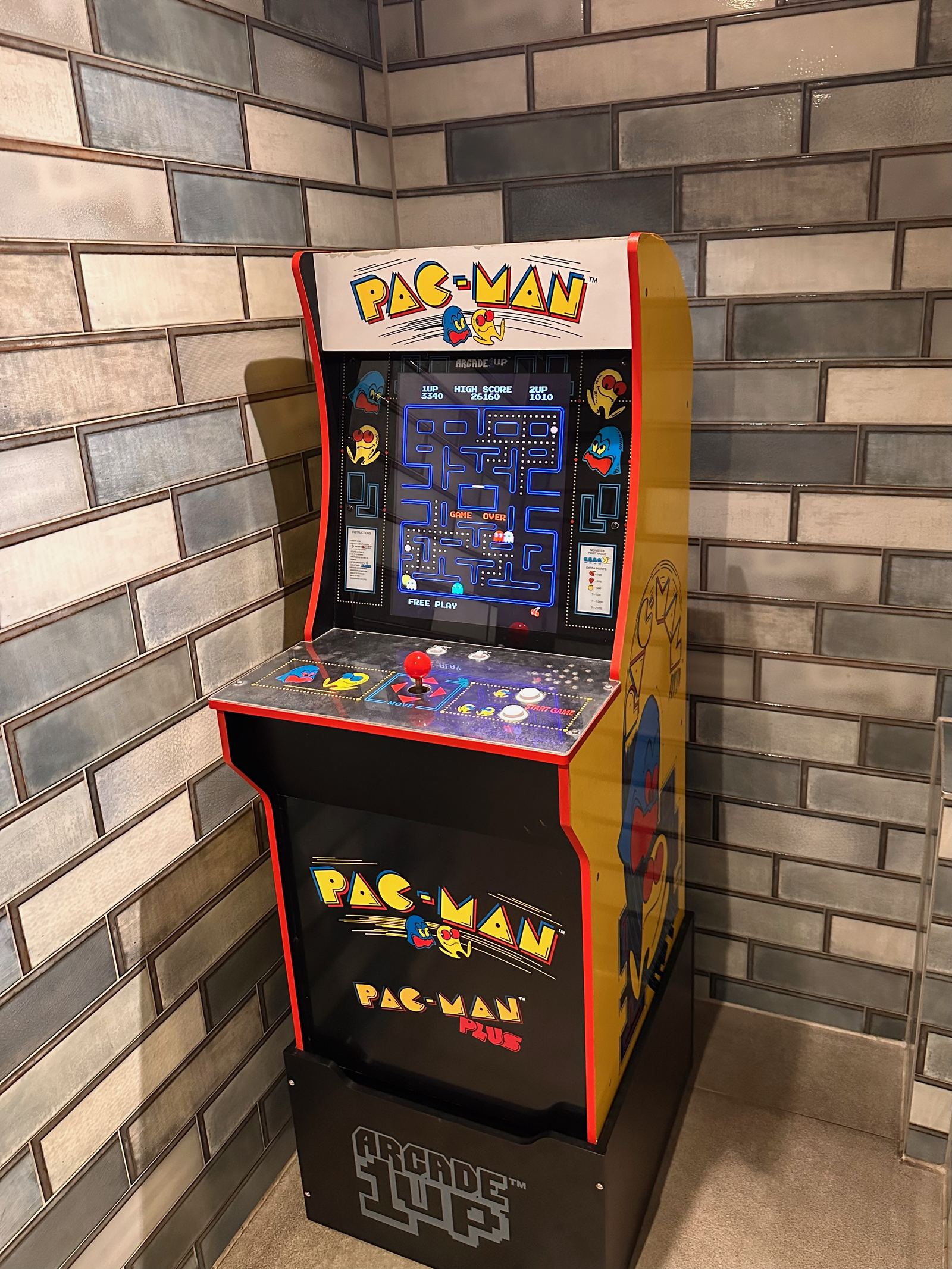 A full-size Pac-Man arcade cabinet with bright yellow side art standing against a brick wall in a cafe