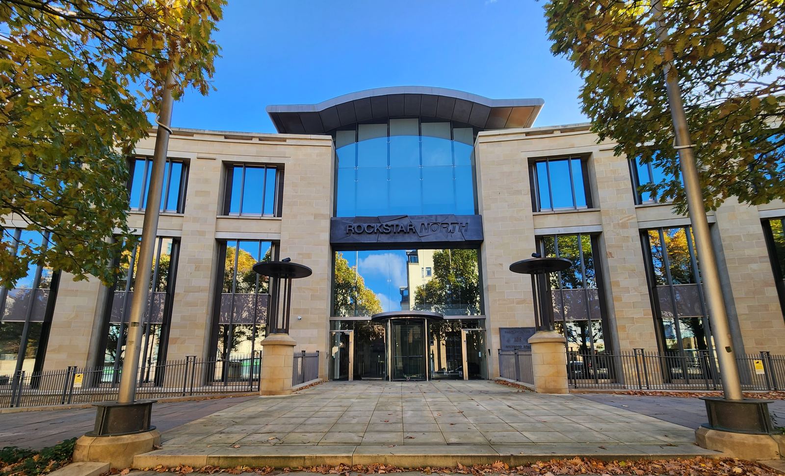 The stone and glass headquarters of Rockstar North in Edinburgh, with a paved plaza and trees in front