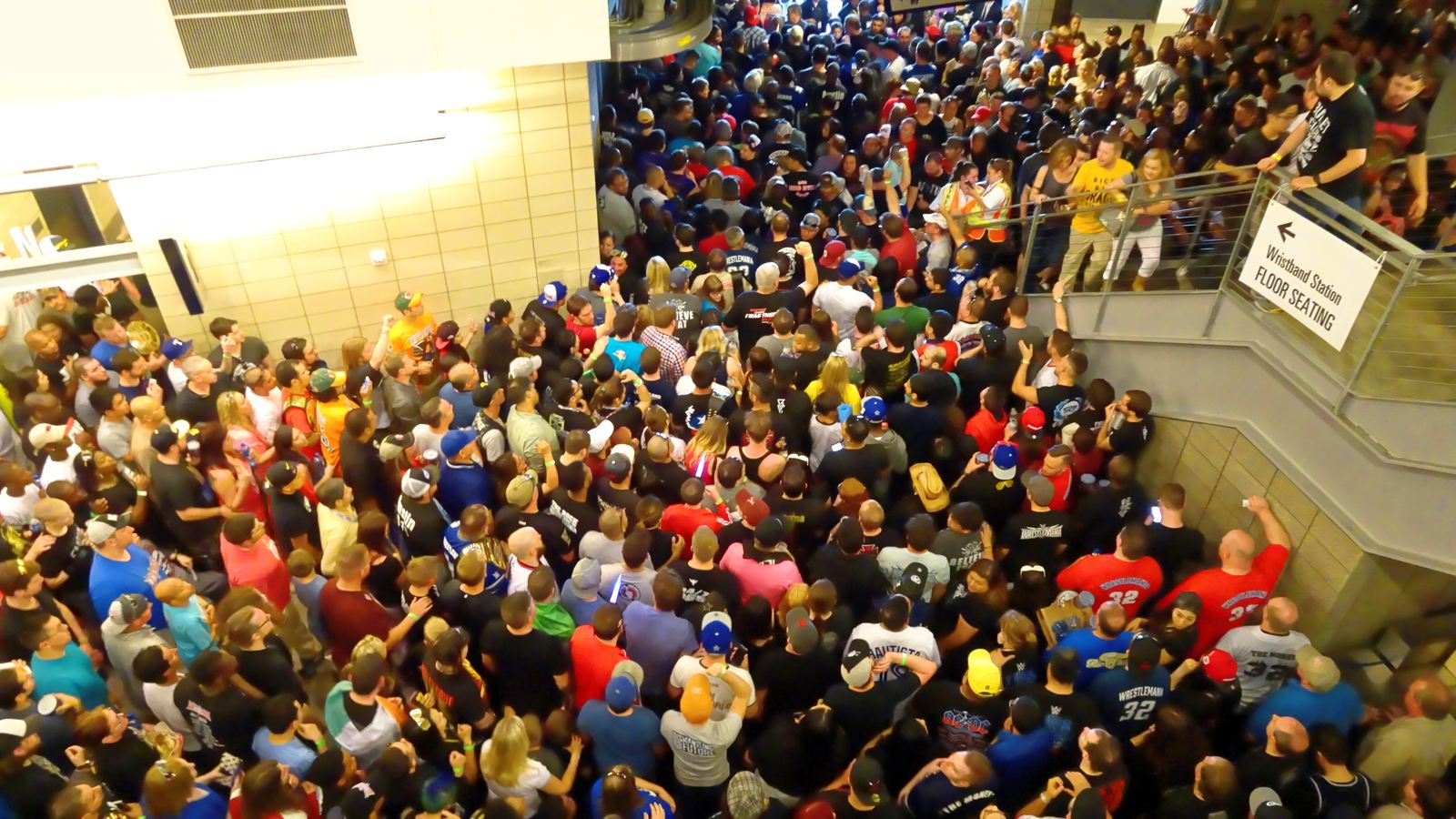 A huge crowd of wrestling fans in colorful shirts filling a stadium concourse on their way into WrestleMania 32